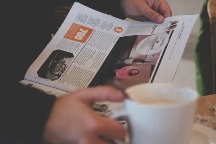 persona leyendo el periódico mientras toma un café